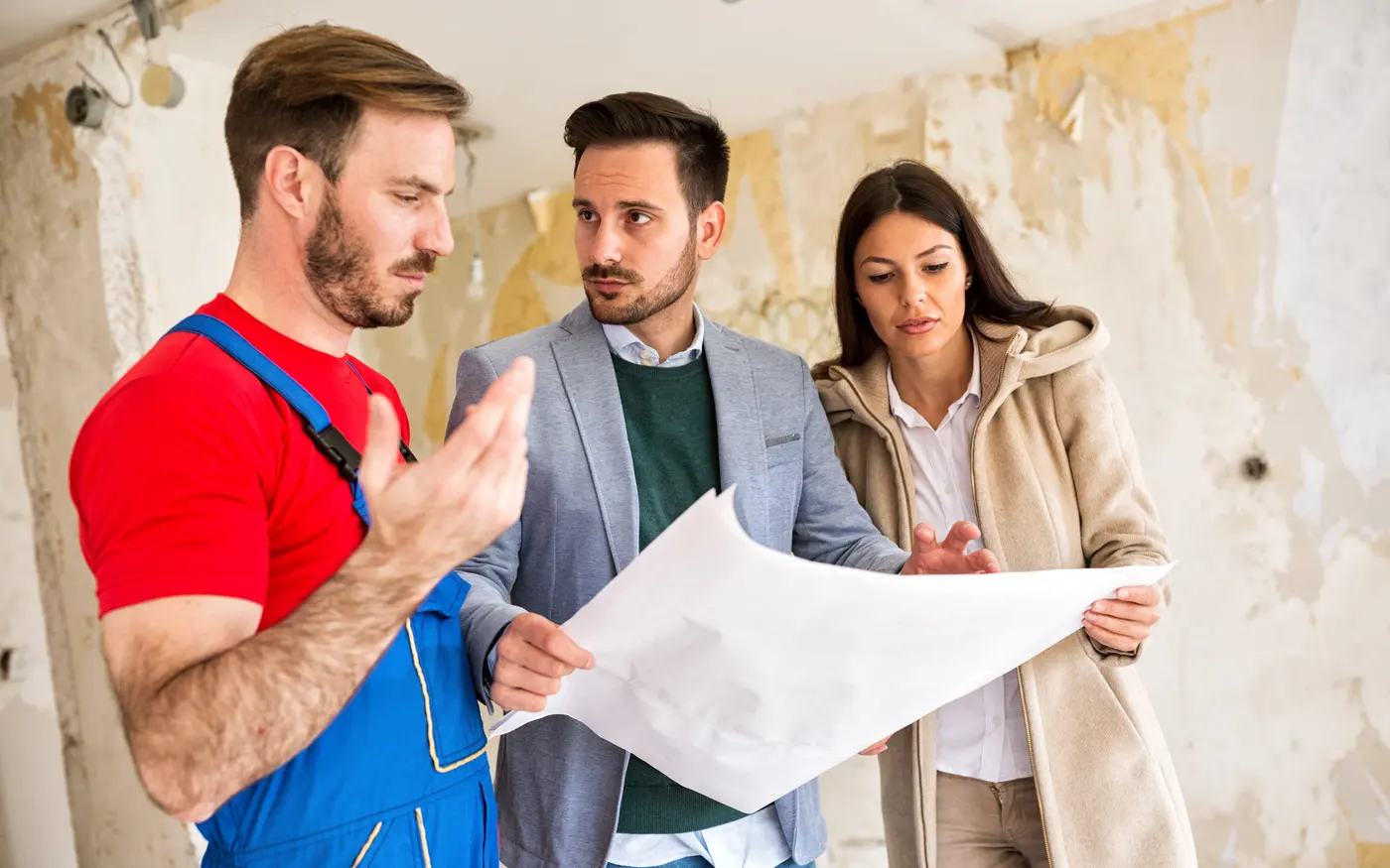 Handwerker bespricht mit einem jungen Paar einen Bauplan in einem Altbau